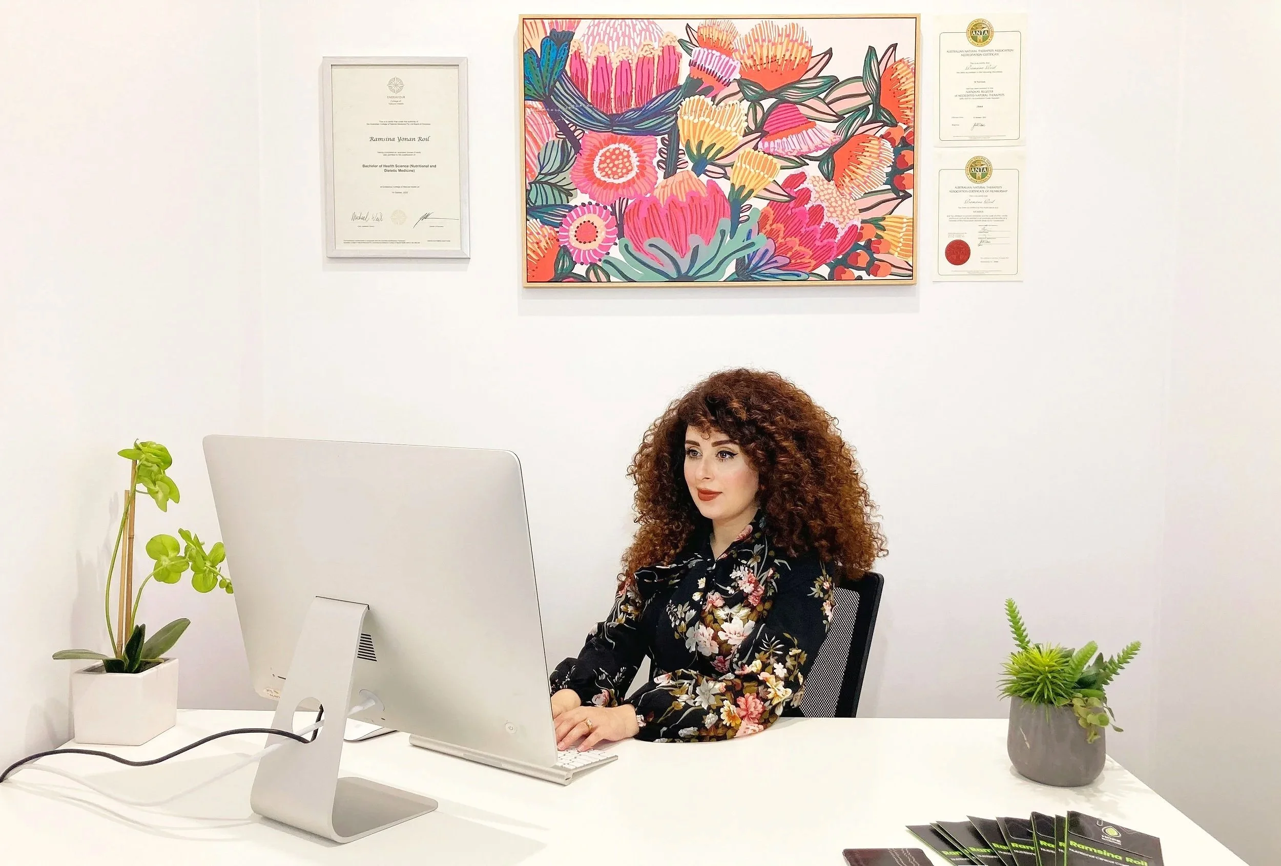 Ramsina at the Hope Nutrition clinic desk with framed qualifications and artwork behind her